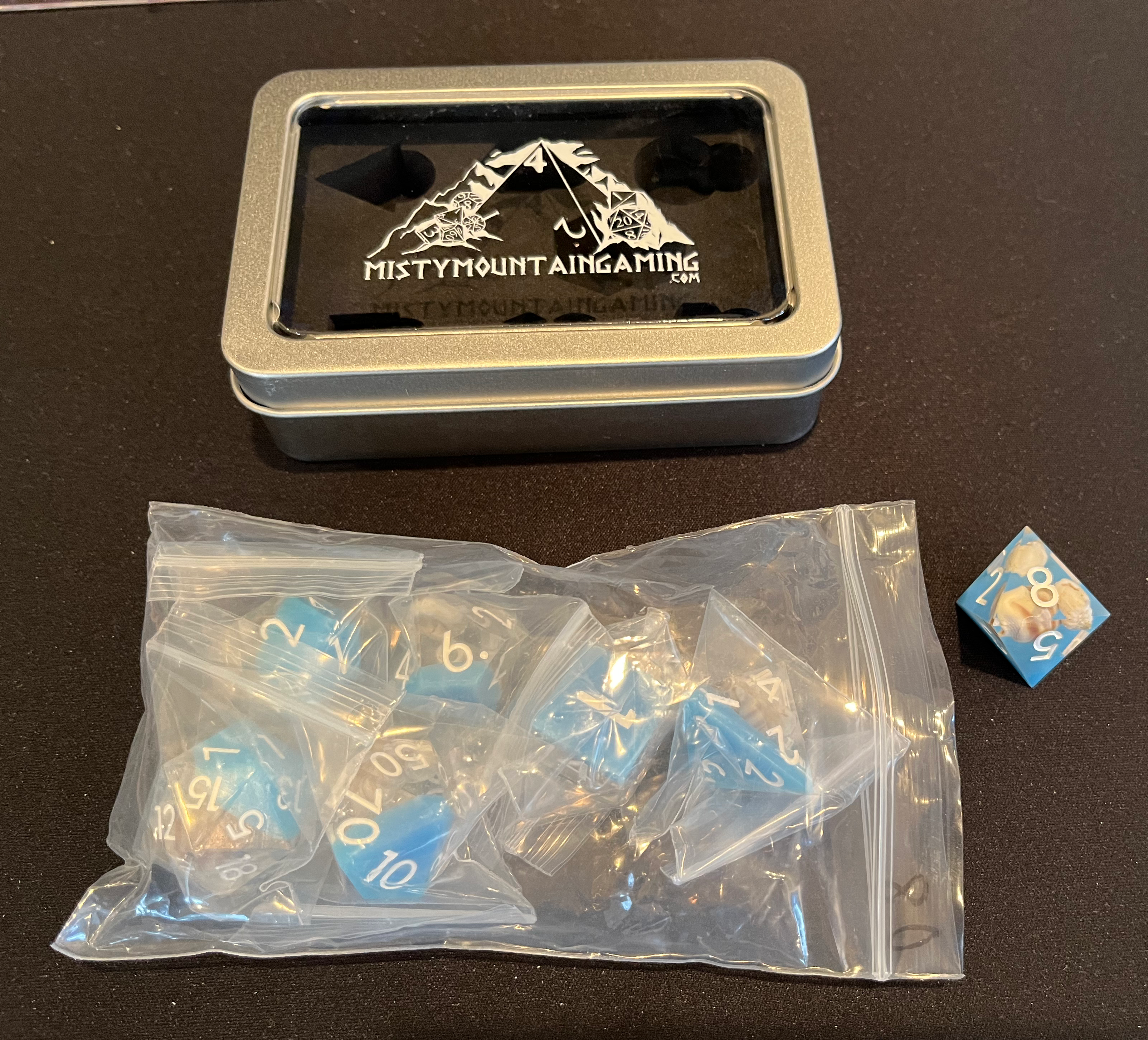 A plastic baggie filled with other, very small plastic baggies, one per die, containing a standard set of 7 roleplaying dice. There is also a small display/storage case with the store logo on top.