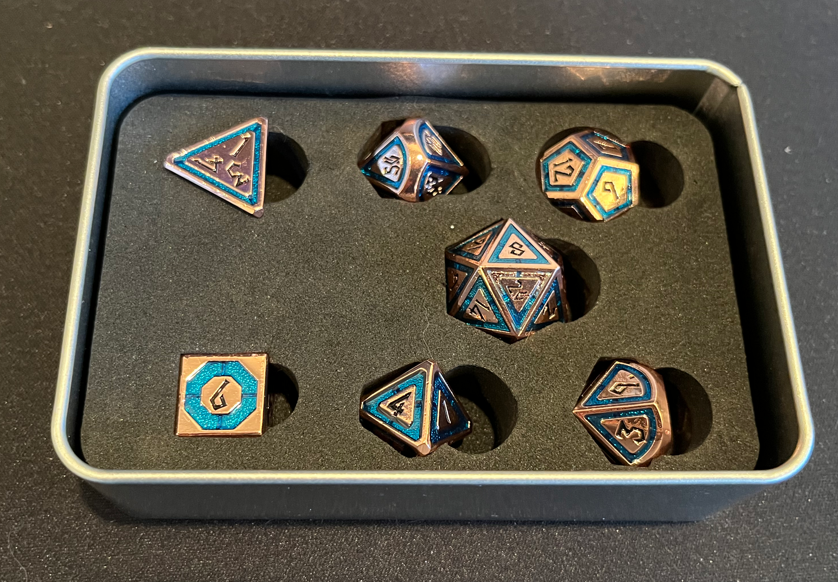 The metal dice, arrayed in an opened storage case, showing how they fit relatively neatly into purpose-cut holes in a foam pad.