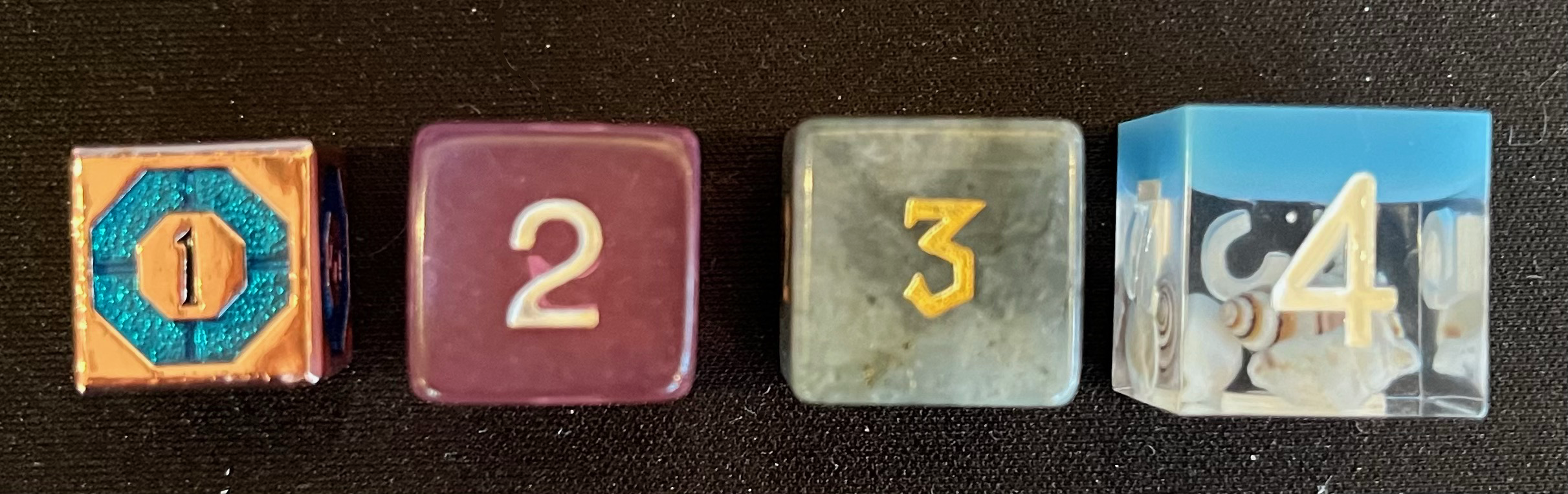 4d6 lined up in size order from above: the metal, the acrylic, the stone, and the resin.